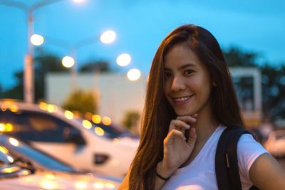 Portrait of smiling young woman standing on street at dusk