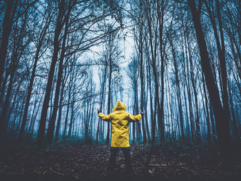 Woman standing by tree trunk in forest