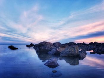 Rocks by sea against sky during sunset