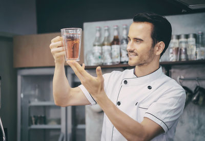 Man holding drink while standing in kitchen