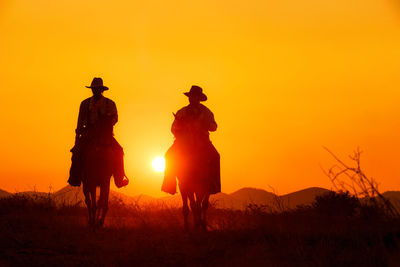 Silhouette people riding on field against sky during sunset