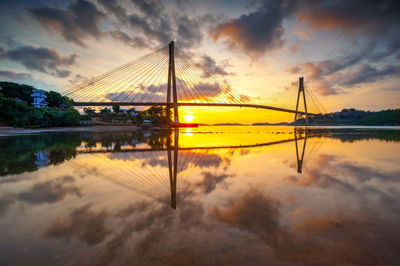 Reflection of bridge on water against orange sky