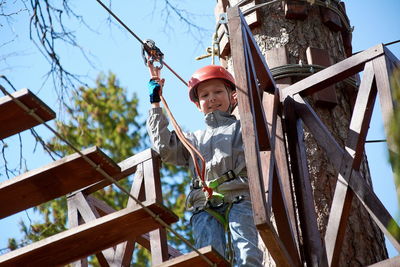 A child in a helmet climbs a rope ladder.