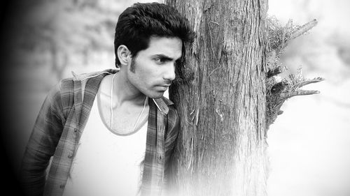 Thoughtful young man looking away while leaning on tree