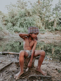 Full length of shirtless man sitting on rock