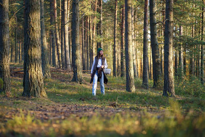 Young woman city dweller gets lost and looks for pathway in huge autumn forest at sunset