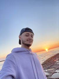 Young man looking away at beach against sky during sunset