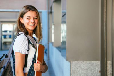 Side view portrait of smiling teenage girl holding books