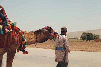 Rear view of man standing by camel at desert