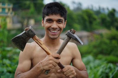 Portrait of young man holding hammer and axe outdoors