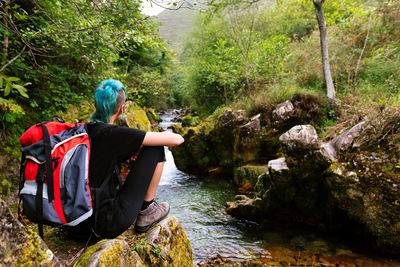 Rear view of woman sitting on rock by river in forest