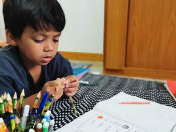 Boy looking at pencil while lying on bed at home