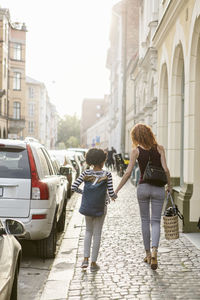 Rear view of woman and daughter walking on sidewalk in city