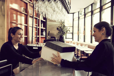 Smiling owner and coworker with modem box at checkout counter in cafe