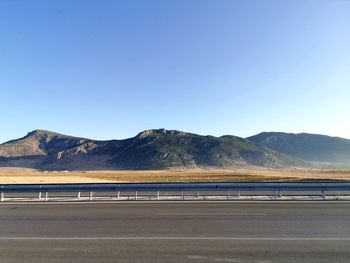 Scenic view of road by mountains against clear blue sky