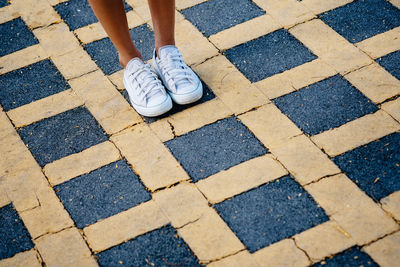 Low section of woman wearing white shoes while standing on patterned road