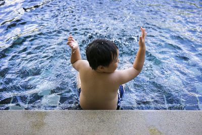 Rear view of shirtless boy swimming in pool