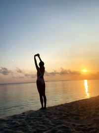 Full length of woman exercising at beach during sunset