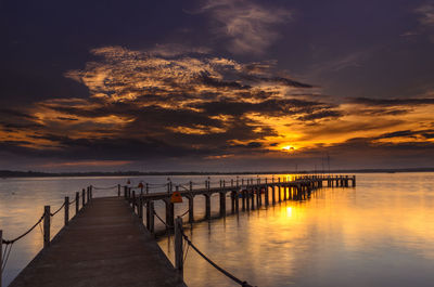 Silhouette pier over sea against cloudy sky during sunset