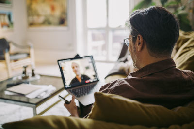 Mature businessman on video call with male colleague in living room during pandemic