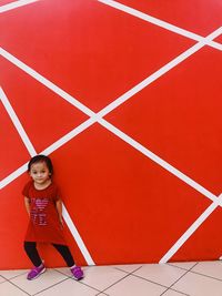 Full length portrait of cute girl against red wall