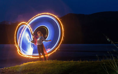 Woman making lighting paintings by lake at night