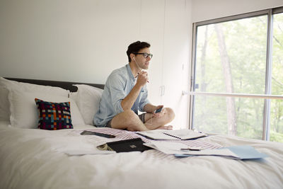 Man talking through headphones from phone while working on bed at home