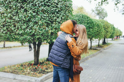 Couple kissing while standing against trees at park