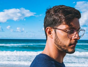 Portrait of young man wearing eyeglasses at beach against sky