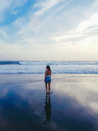 Full length rear view of woman standing at beach against sky