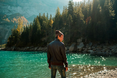 Rear view of hiker standing by against trees by river