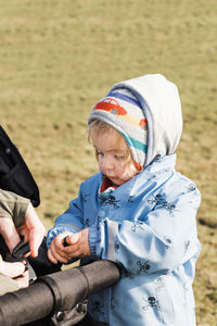 Cute baby boy in warm clothing standing on field