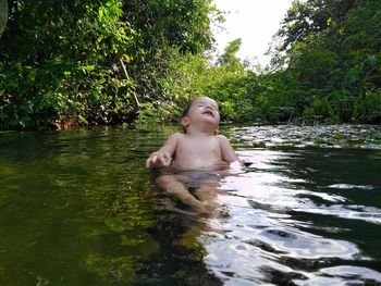 Shirtless boy in lake against trees