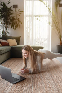 Girl doing yoga exercises at home with green loft interior watching and repeating trainer exercises