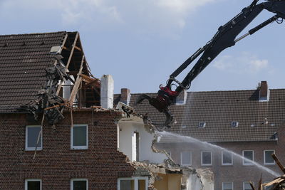 Bulldozer demolishing house against sky