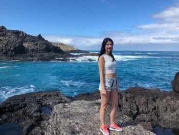 Portrait of young woman standing on beach against sky