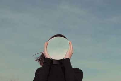 Woman holding mirror against sky