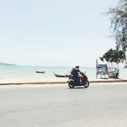 Man riding motor scooter on road by beach