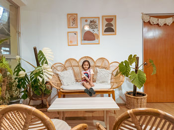 Happy little girl sitting on the rattan couch in a boho interior design.