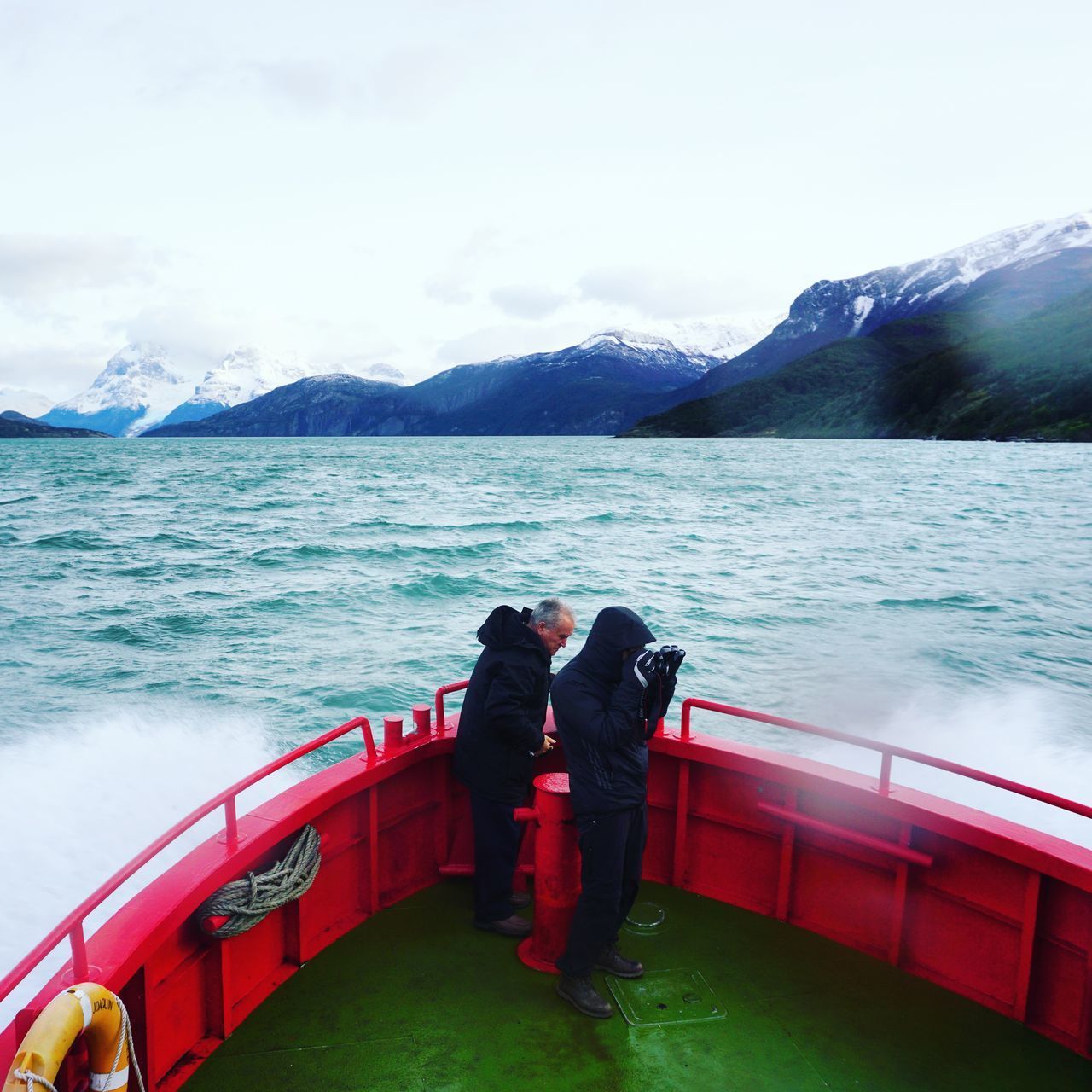 REAR VIEW OF MEN LOOKING AT SEA AGAINST MOUNTAIN