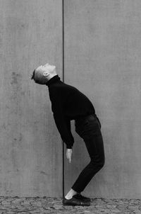 Side view of young man bending while standing on footpath by wall