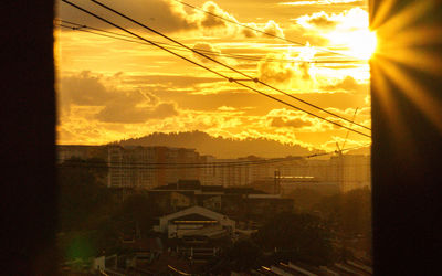 Silhouette of electricity pylon in city during sunset