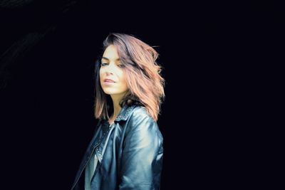 Portrait of young woman against black background