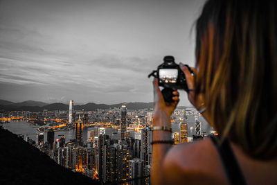 Rear view of woman photographing cityscape against sky