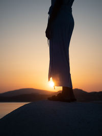 Woman standing by sea against sky during sunset
