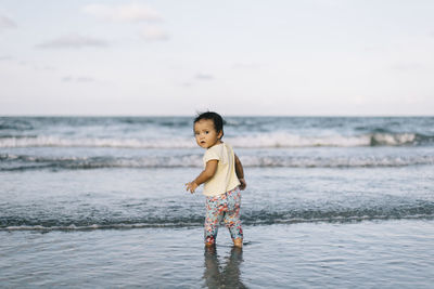 Baby girl standing at beach against sky