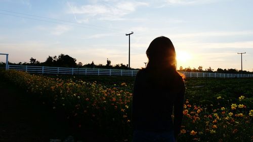 Rear view of woman standing on field against sky