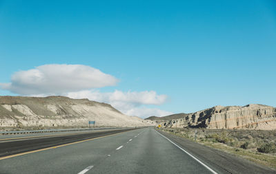 Empty road by mountains against blue sky