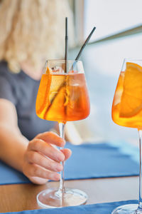 Blurred background, adult woman holding an aperol spritz cocktail, lunch in a cafe, selective focus