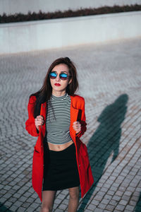 Portrait of beautiful young woman in sunglasses standing on footpath